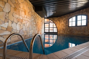 An indoor swimming pool with stone walls and a view through arched windows.