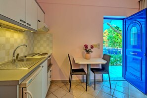 A compact kitchen with a sink, stove, and cabinets, a small dining table with chairs, and a view of a balcony with a blue door.