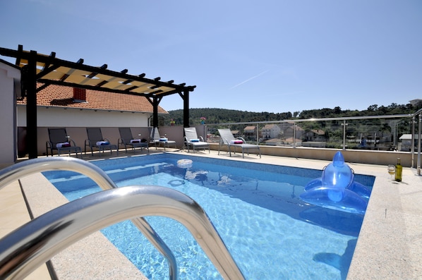 Relax by the pool with a clear view of the surrounding landscape, featuring a tiled deck, lounge chairs, and a covered seating area.