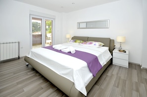 Relax in this serene bedroom with a large bed, white nightstand, and a peaceful view of lush greenery.