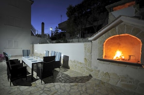 Enjoy al fresco dining in a serene outdoor setting with a fireplace and comfortable wicker chairs.