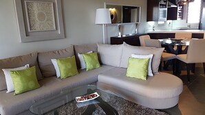 A modern living room with a sectional sofa, a glass coffee table, and a dining area with a table and chairs. - Apartment in Hotel Residence (Grand-Baie)