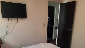 Une chambre à coucher avec un lit, un téléviseur fixé au mur et une porte donnant sur une autre pièce.