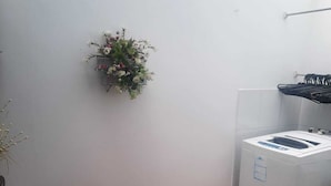 Une petite buanderie comprenant un lave-linge, un étendoir en métal et une plante en pot accrochée au mur.