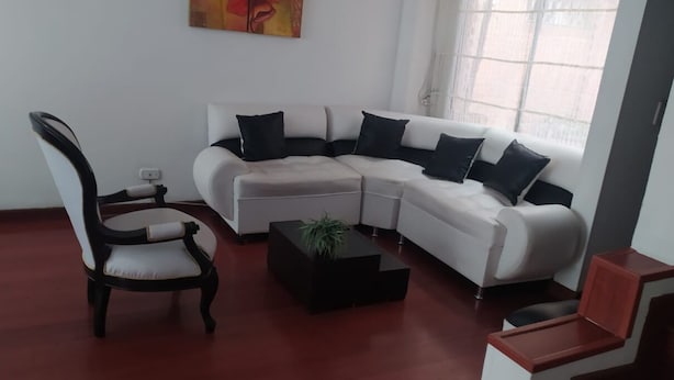 Un salon avec un canapé d’angle blanc, une chaise en bois et une table basse noire.
