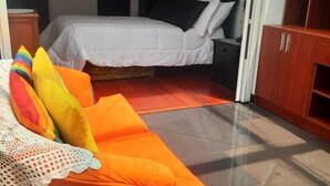 Une chambre à coucher avec un lit, une armoire en bois et un canapé orange vif agrémenté de coussins colorés.