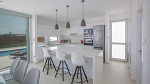A modern kitchen with a large island, bar stools, pendant lights, and a view of the outdoors. - Protaras Holiday Villa Bp13 (Paralimni)