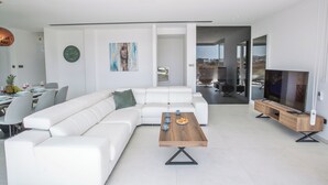 A modern living room with a white sectional sofa, a wooden coffee table, and a flat-screen TV on a wooden stand. - Protaras Holiday Villa Bp13 (Paralimni)
