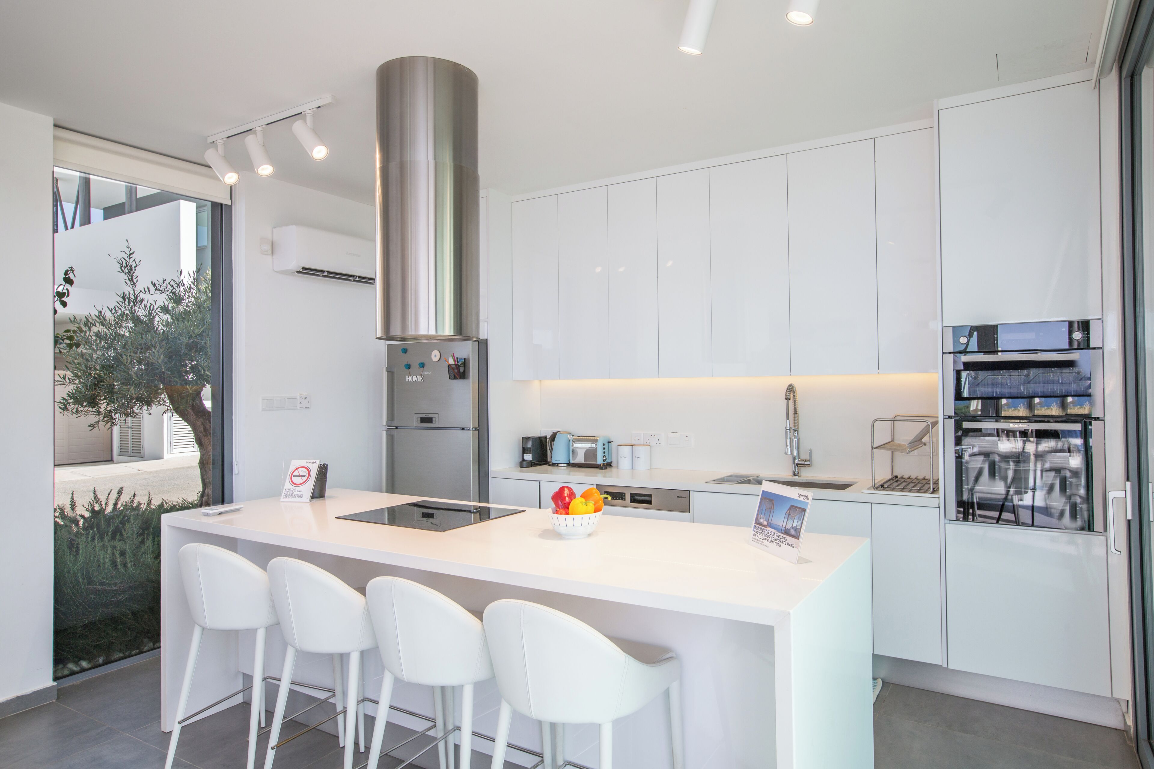 A modern kitchen with white cabinetry, a stainless steel range hood, and a central island with bar stools.