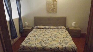 A bedroom with a bed, two bedside tables, a wall-mounted artwork, and curtains.