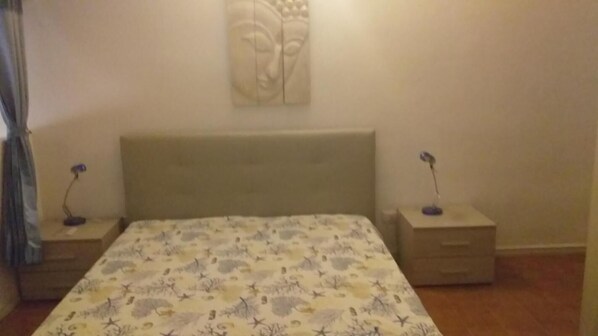 A bedroom with a bed, two bedside tables, a nightstand, a wall-mounted artwork, and a window with curtains. - Villa Lunetta 300 Meters From the Beach (Villasimius)