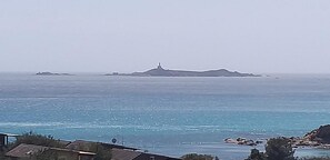 Vista costera con una isla destacada y un faro a lo lejos.