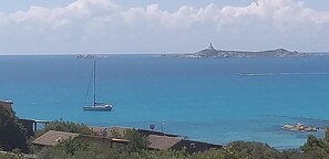 Vista costera con un velero, edificios y una isla distante.