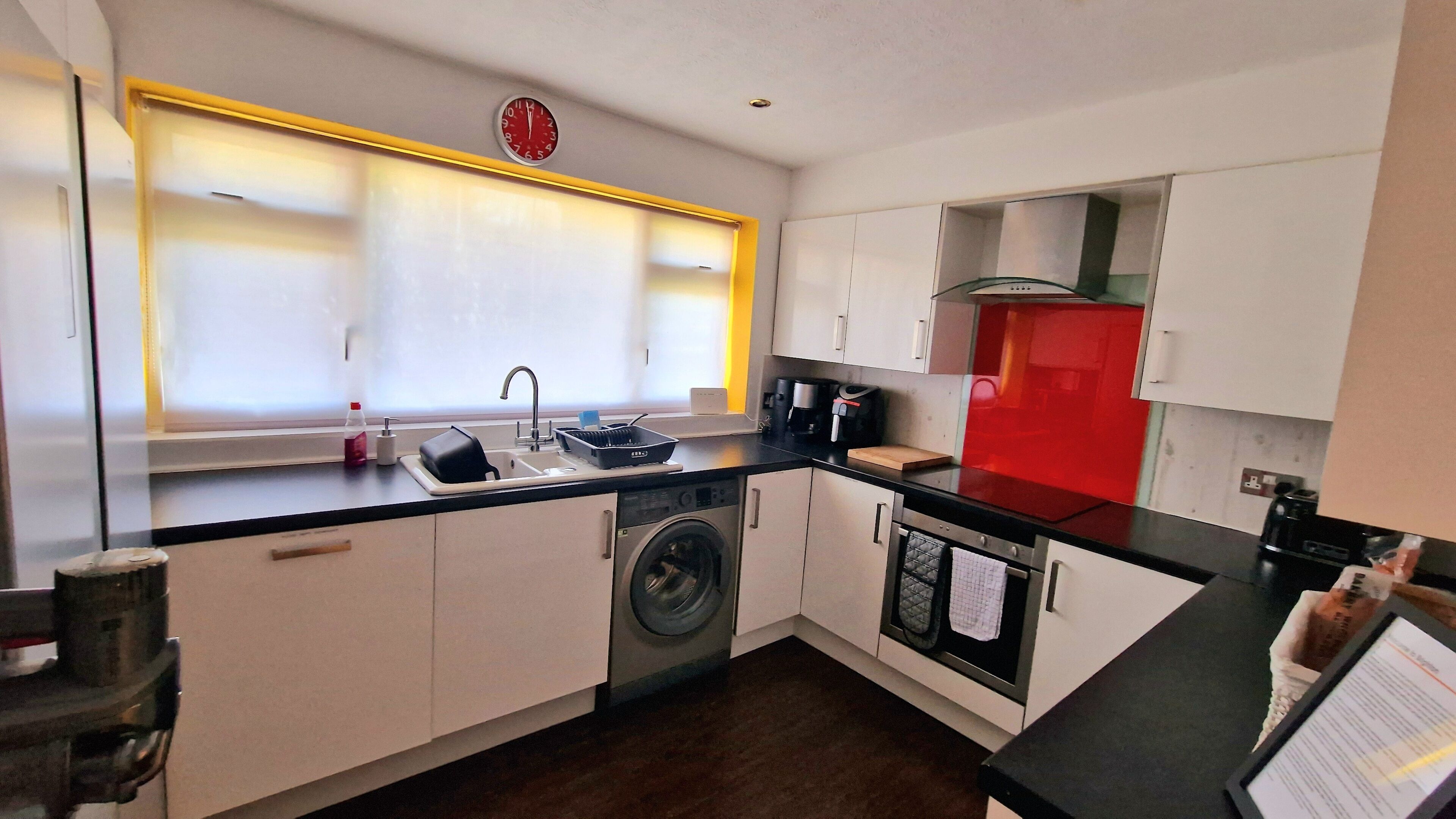 A compact kitchen with a washing machine, a sink, a coffee maker, and a red cabinet.
