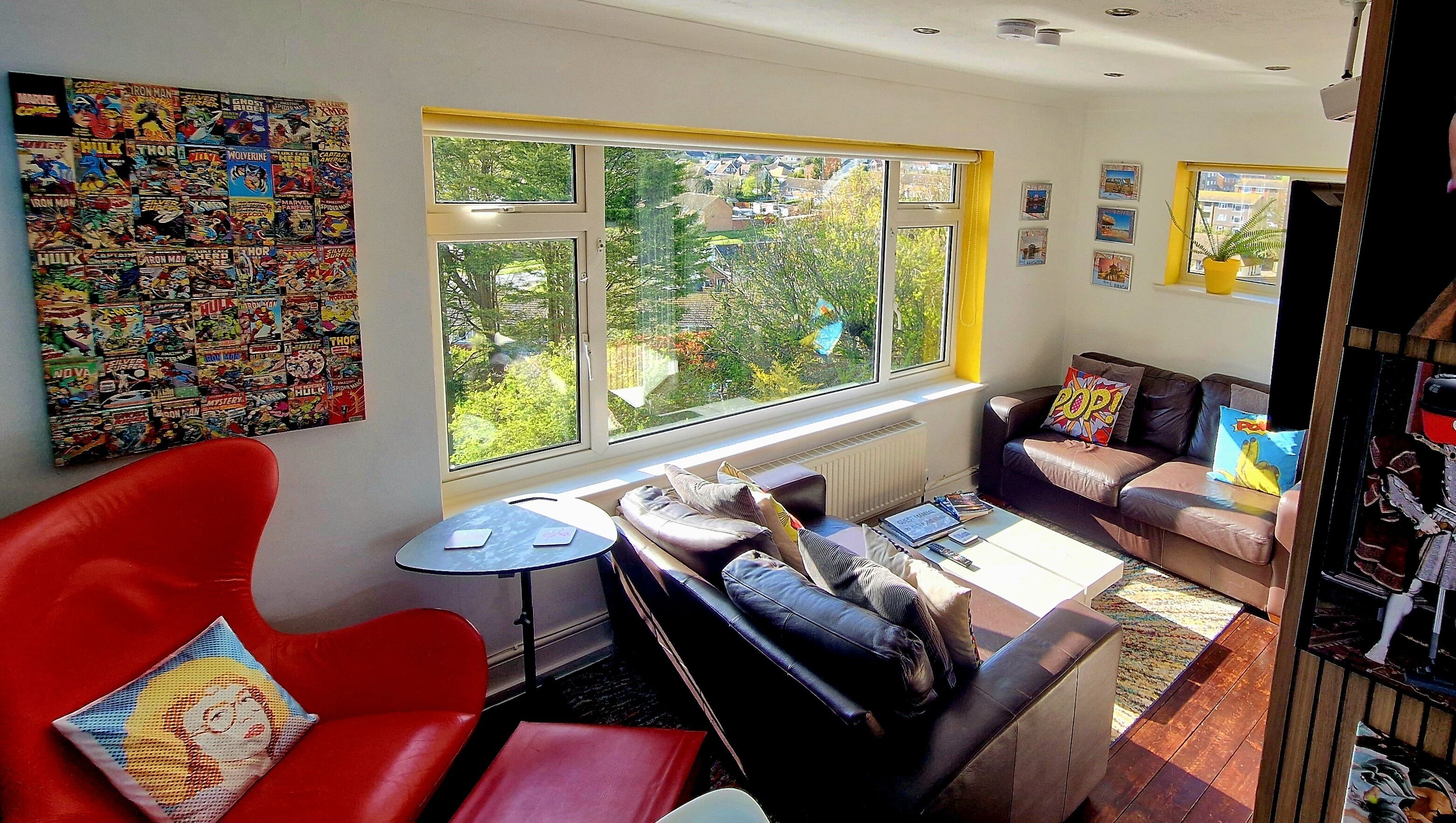 A living room with a red chair, a sofa, a small table, and a window with a view of greenery.