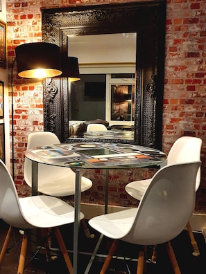 Een ronde glazen tafel met vinylplaten, omringd door witte stoelen, in een kamer met openliggende bakstenen muren en een grote, versierde spiegel.