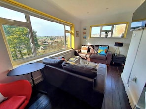 Een moderne woonkamer met een bank, een rode stoel, een bijzettafeltje en een televisie.