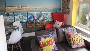 A room with a view of the sea, a red armchair, a sofa with colorful pillows, and a table with a chair. - 3 Bed House Stunning Views And Free Parking (Brighton)