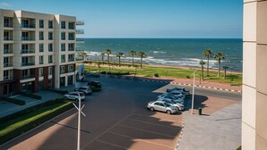 A modern hotel with a parking lot, a view of the ocean, and a landscaped area with palm trees. - Luxurious Chalet in Port Said Governorate With Views (Al-Manasrah)
