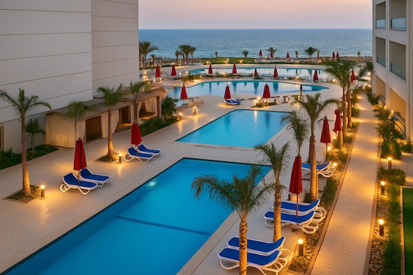 A resort pool area with multiple swimming pools, lounge chairs, and umbrellas.