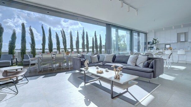 A modern living room with a large window, a grey sofa, and a dining area. - Protaras Holiday Villa Wp8 (Paralimni)