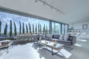 A modern living room with a large window, a grey sofa, and a dining area. - Protaras Holiday Villa Wp8 (Paralimni)