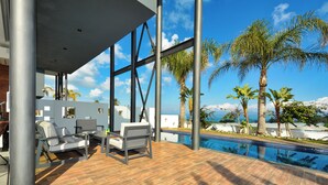 A modern outdoor pool area with a wooden deck, lounge chairs, and a view of the ocean. - Protaras Holiday Villa Wp8 (Paralimni)