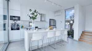 A modern kitchen with white cabinetry, stainless steel appliances, and a central island with bar stools. - Protaras Holiday Villa Wp8 (Paralimni)