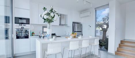 A modern kitchen with white cabinetry, stainless steel appliances, and a central island with bar stools.