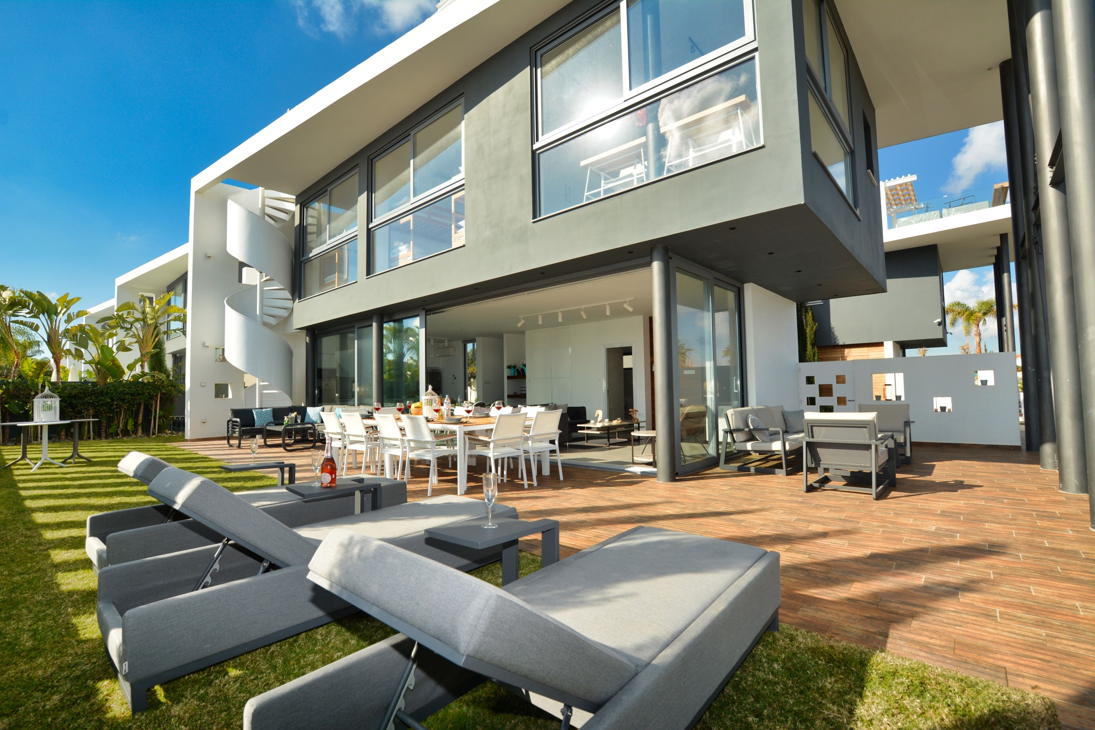 Una casa moderna de dos pisos con un patio que incluye mobiliario exterior y una escalera en espiral.
