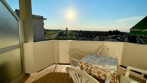 A balcony with a table and chairs, a view of a cityscape, and a clear sky. - Cozy Studio With Balcony-beahost (Caorle)