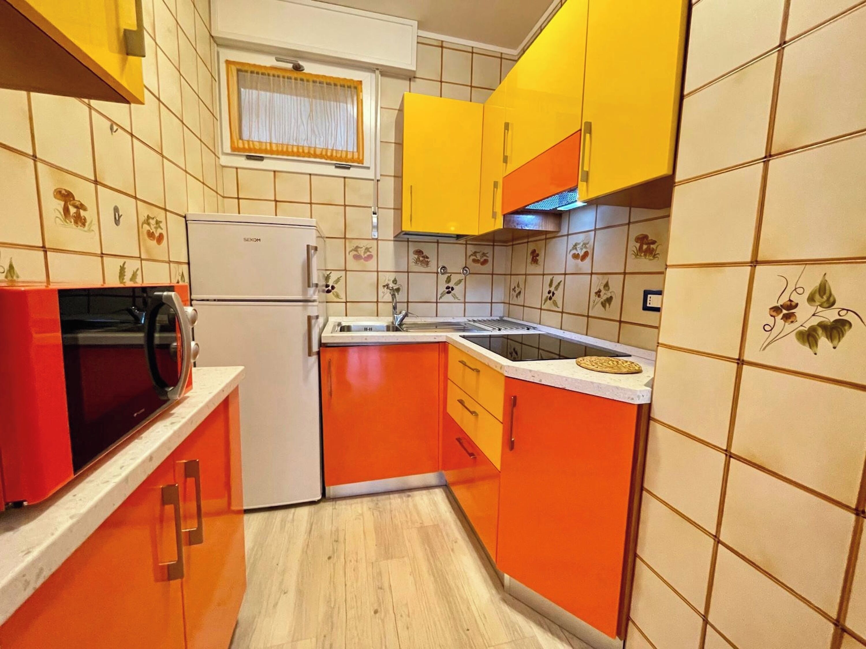 Keittiössä on oranssit kaapit, valkoinen jääkaappi ja mikroaaltouuni.