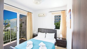 Une chambre d’hôtel avec un balcon, un lit avec du linge de lit blanc, une table de chevet et une fenêtre avec des rideaux.