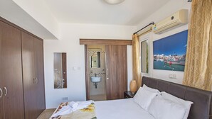 Une chambre d’hôtel avec un grand lit, une armoire, une salle de bain avec un lavabo et un tableau représentant un port accroché au mur.