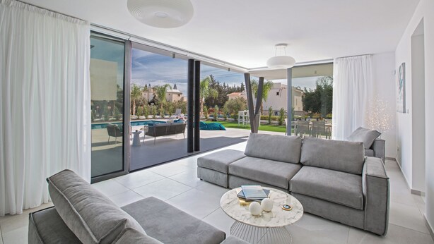 Una sala moderna con un sofá gris, una mesa de centro y vistas a una piscina y zona de estar al aire libre.