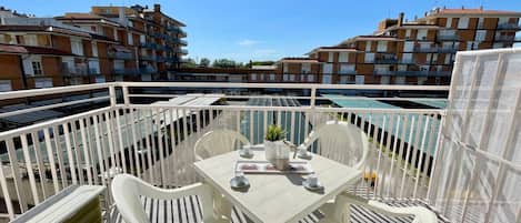 A balcony with a table and chairs, a striped awning, and a view of residential buildings.