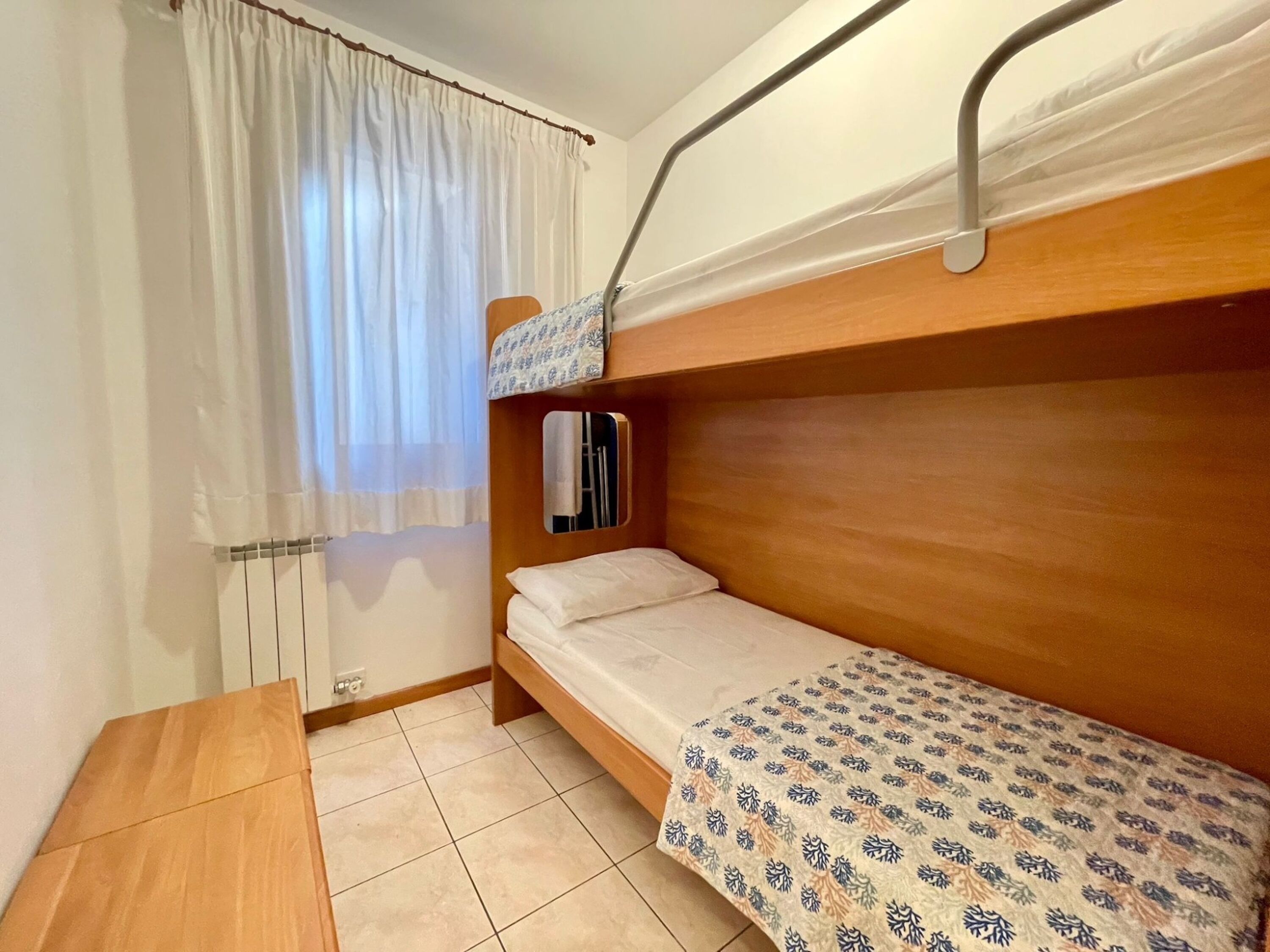 Un alojamiento pequeño y de una sola habitación con literas, una mesita y una ventana con cortinas.
