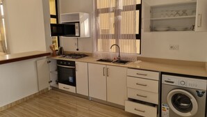 Une cuisine compacte équipée d’une cuisinière à gaz, d’un four à micro-ondes, d’un évier et d’un lave-linge encastré.