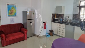 A compact living space with a kitchenette, a red sofa, a purple bed, and a map on the wall. - Studio Solitaire Ideal for two Adults - Garden View 1 (Trou aux Biches)