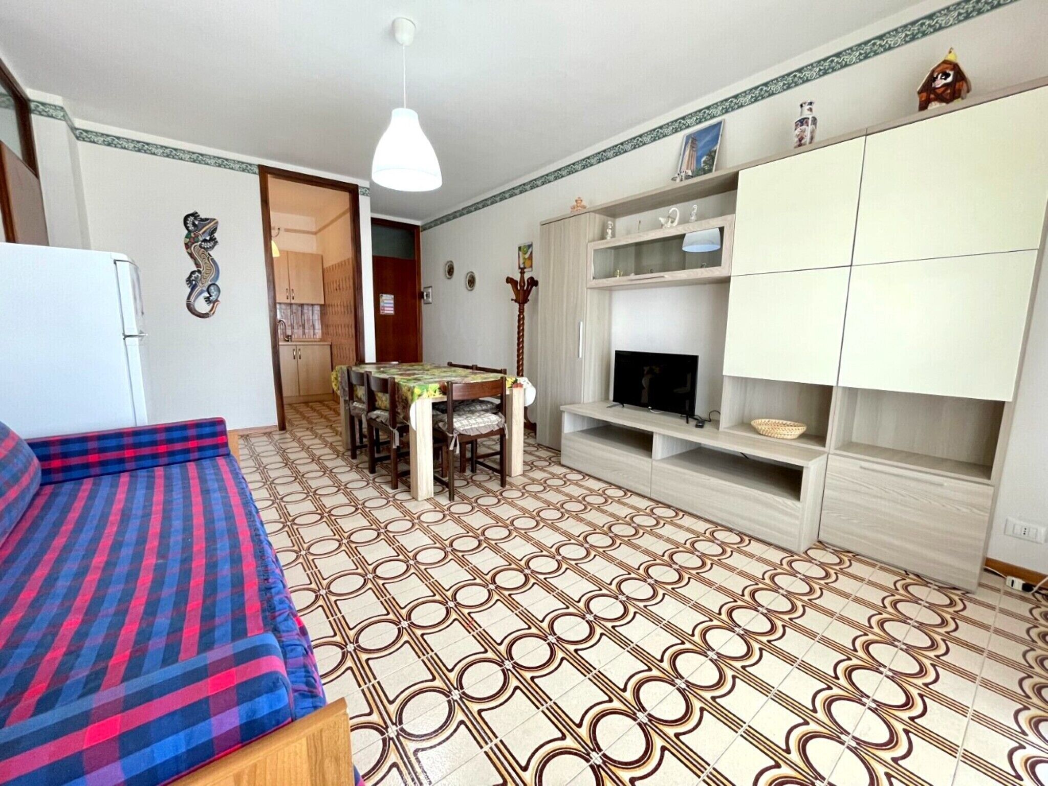 A compact living space with a sofa, dining table, TV stand, and patterned floor tiles.