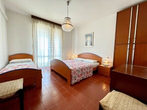 A bedroom with two single beds, a wooden wardrobe, a desk, and a hanging light fixture. - Comfy Flat With Terrace 250mt From the sea (Caorle)