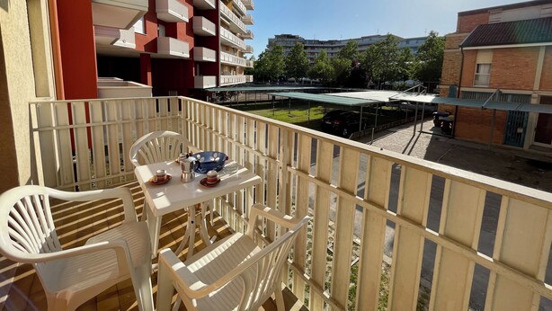 En balkon med hvide plastikstole og et bord, der ud til et parkeringsområde og bygninger.