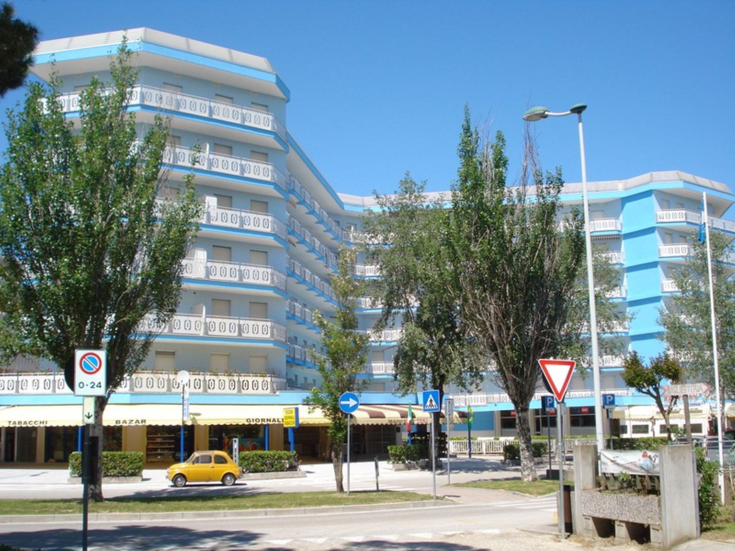 Un hotel de varios pisos con balcones, un paso de peatones y una señal de no estacionamiento.
