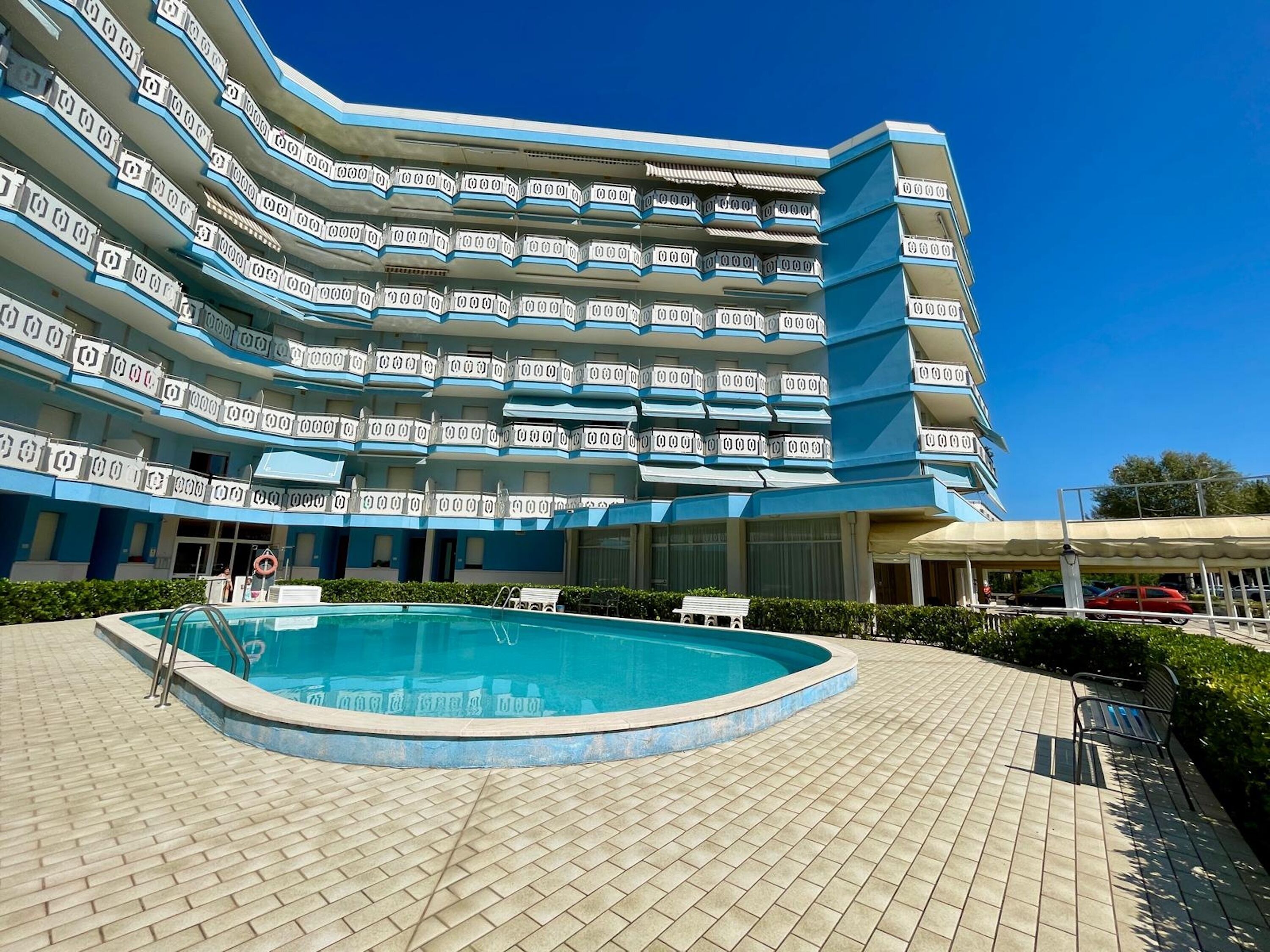 Un hôtel à plusieurs étages doté d’une piscine et d’un espace extérieur aménagé avec des sièges, protégé par un toit.