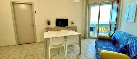 Una sala de estar con una mesa de comedor, sillas, un sofá, un televisor y un balcón con vistas.
