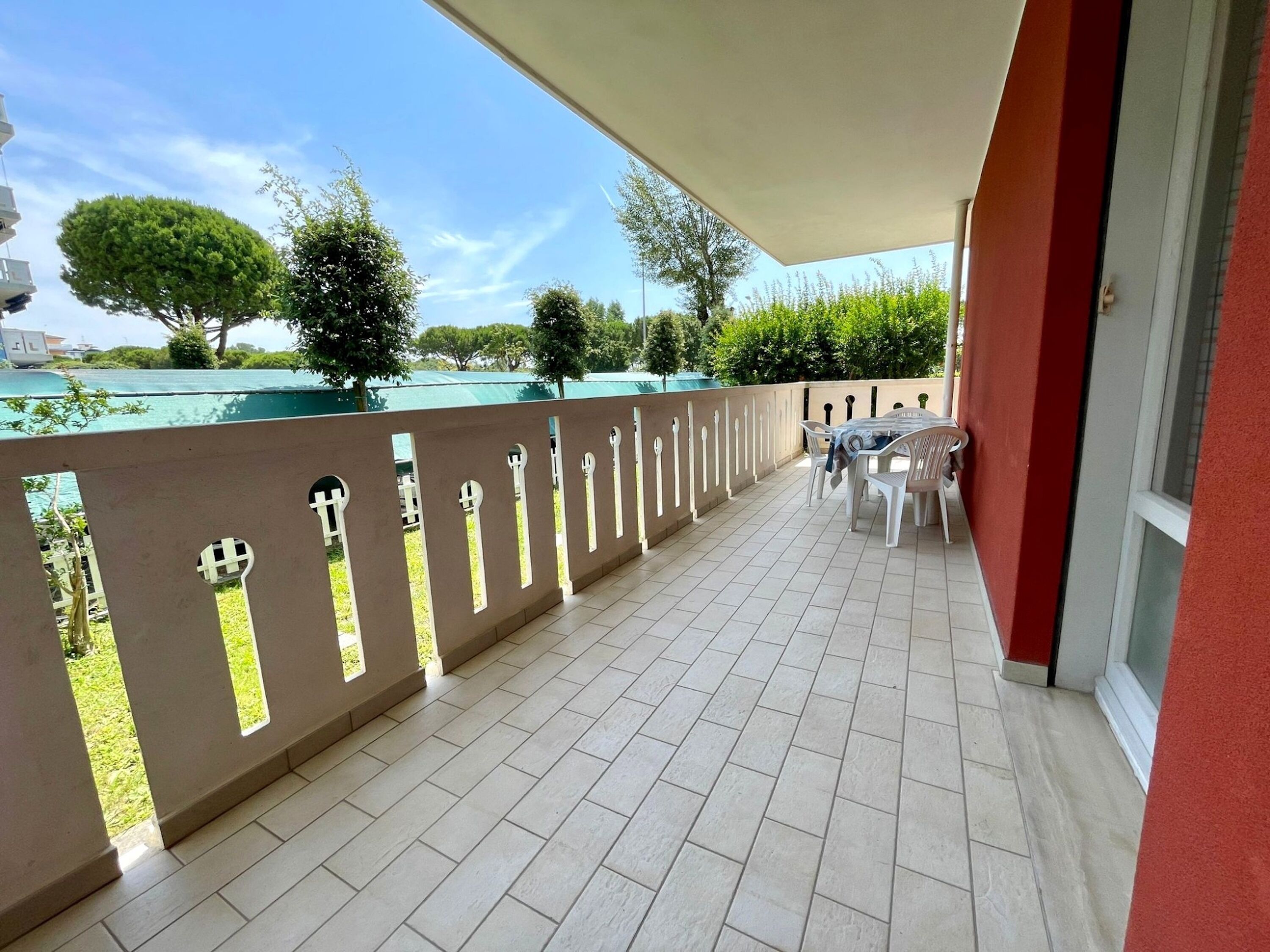 Ein Balkon mit Fliesenboden, Tisch und Stühlen sowie Blick auf Grünflächen und ein Gewässer.