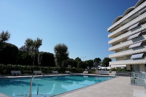 A swimming pool with a clear blue sky, surrounded by a multi-story building with balconies.
