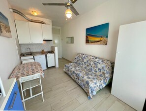 Un espacio habitable compacto con kitchenette, un sofá, una mesa de comedor y un ventilador de techo.