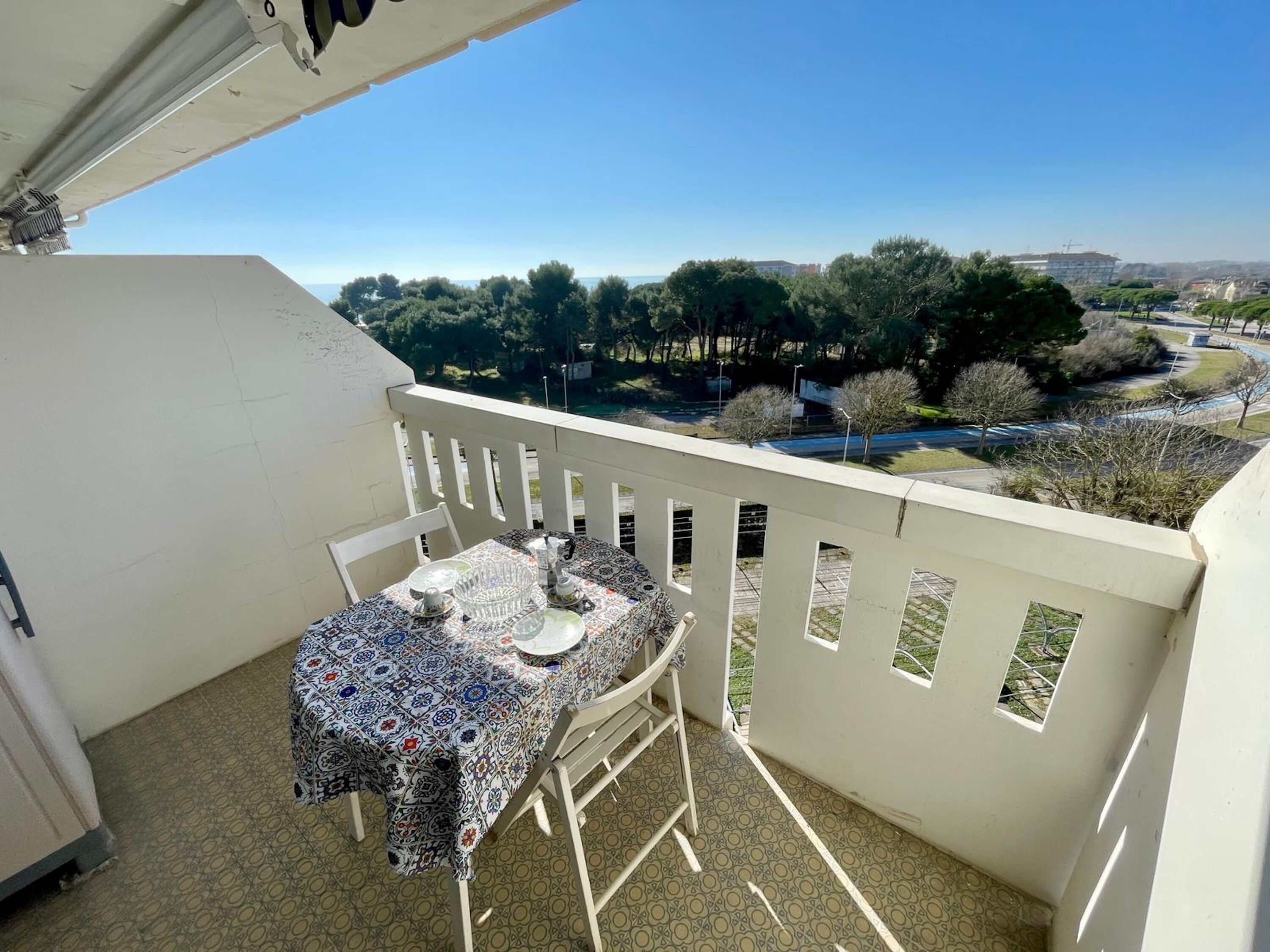 A balcony with a table set for two, overlooking a residential area with trees and a road.