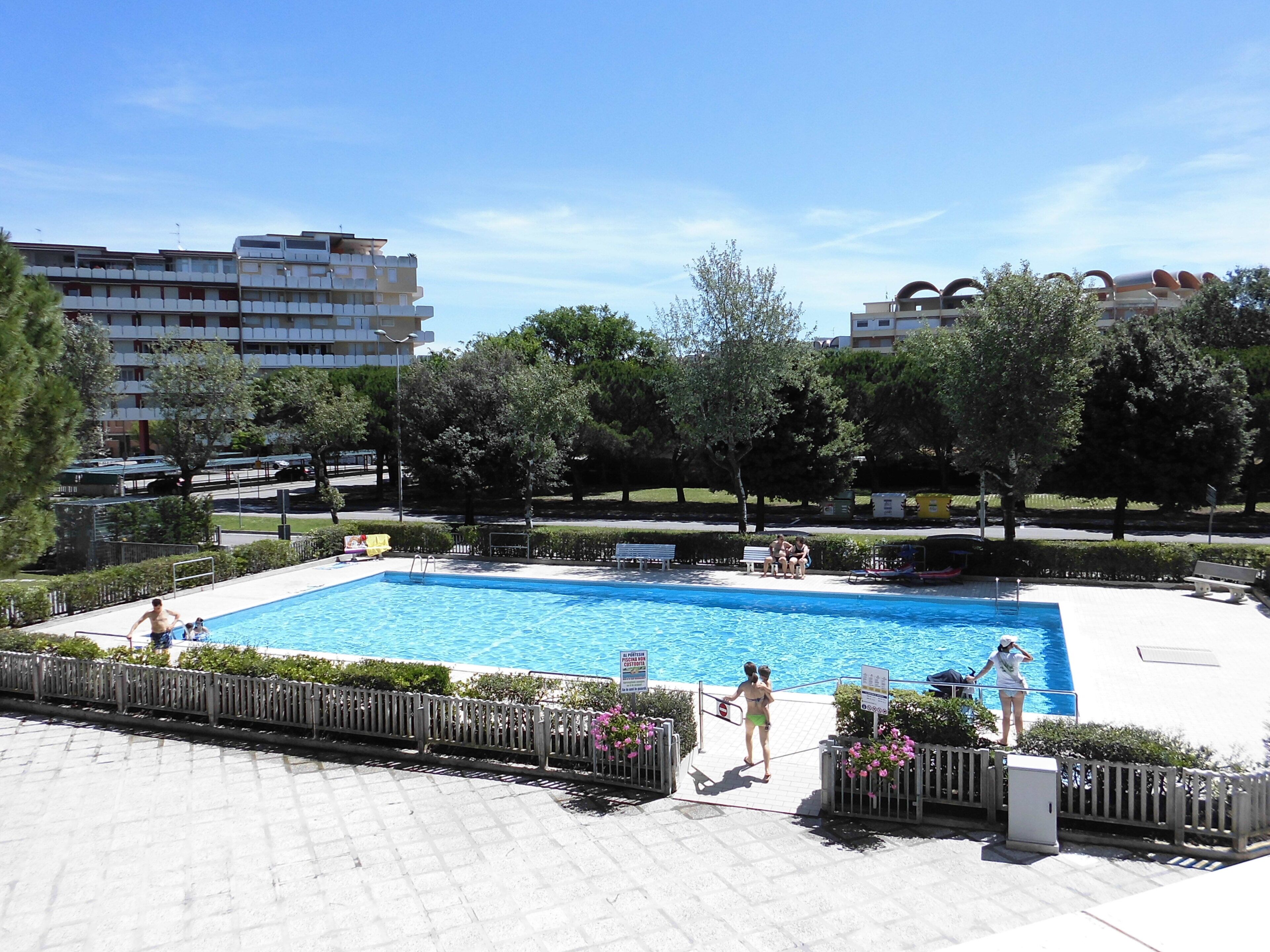 A swimming pool with a paved deck, surrounded by trees and a fence.